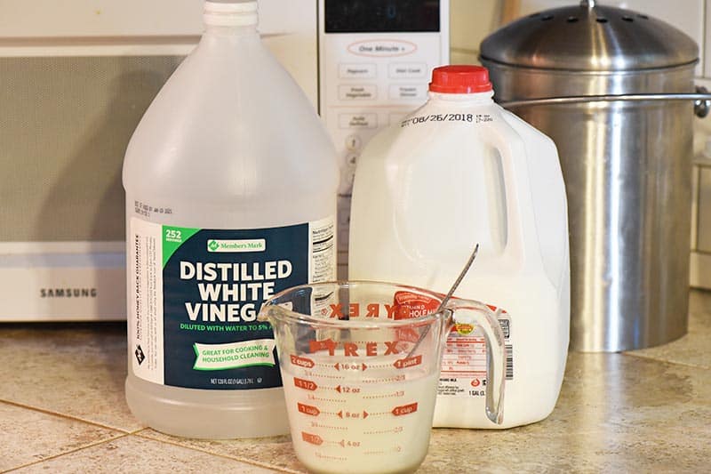ingredients to make buttermilk for chocolate cupcakes recipe, including vinegar and whole milk, with Pyrex measuring cup on tile counterop