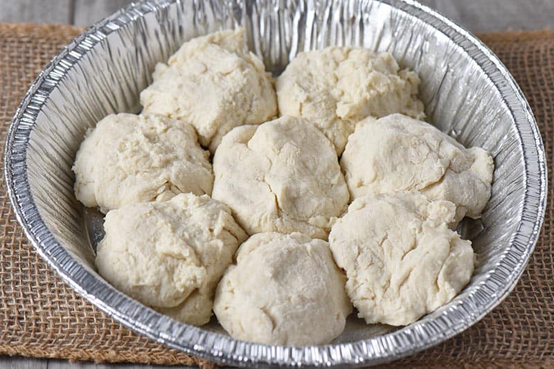 uncooked drop biscuits in a tin foil pie plate for campfire cooking