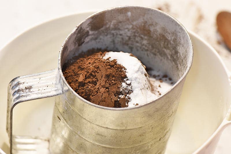 sifting dry ingredients for chocolate cupcakes into white batter bowl