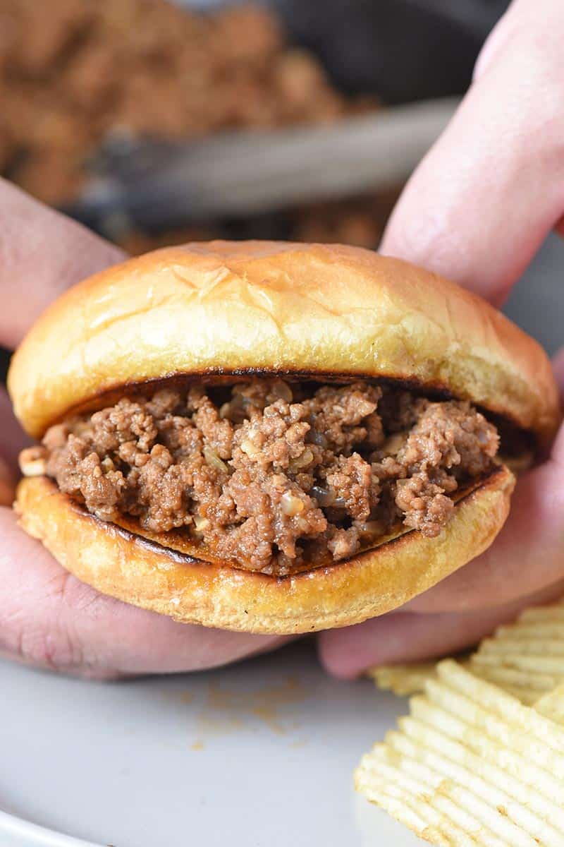 holding a sloppy joe or juicy burger with 2 hands above a plate of potato chips