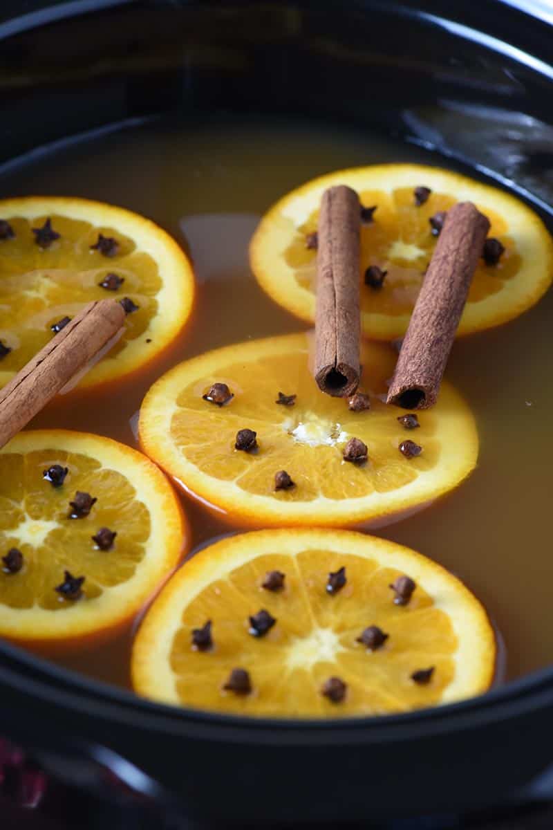 mulled cider with orange slices, whole cloves, and cinnamon sticks in black slow cooker
