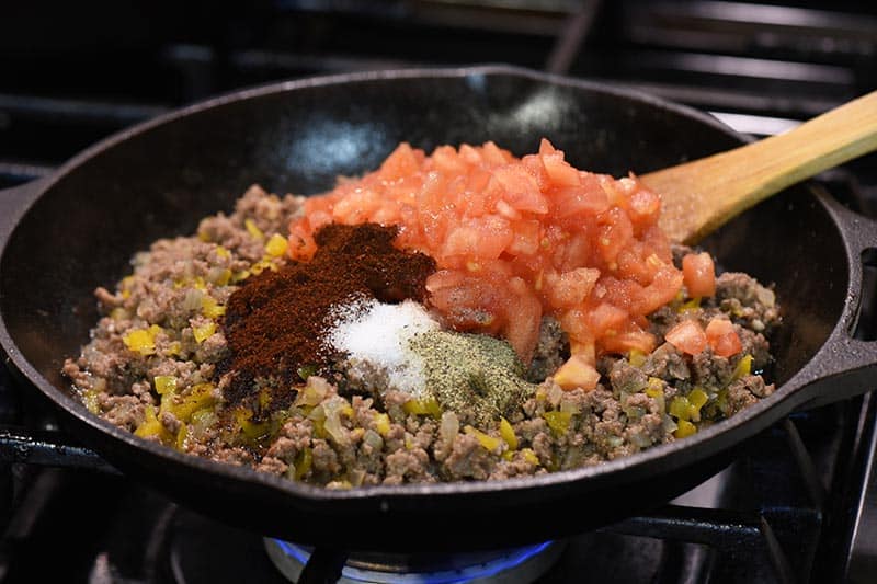 adding ingredients for taco seasoning to taco sloppy joes meat in cast iron skillet on stovetop