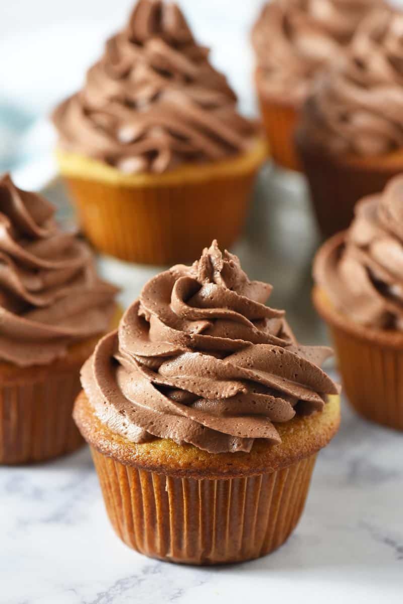 swirled chocolate frosting for piping on yellow cake cupcakes on white marble countertop