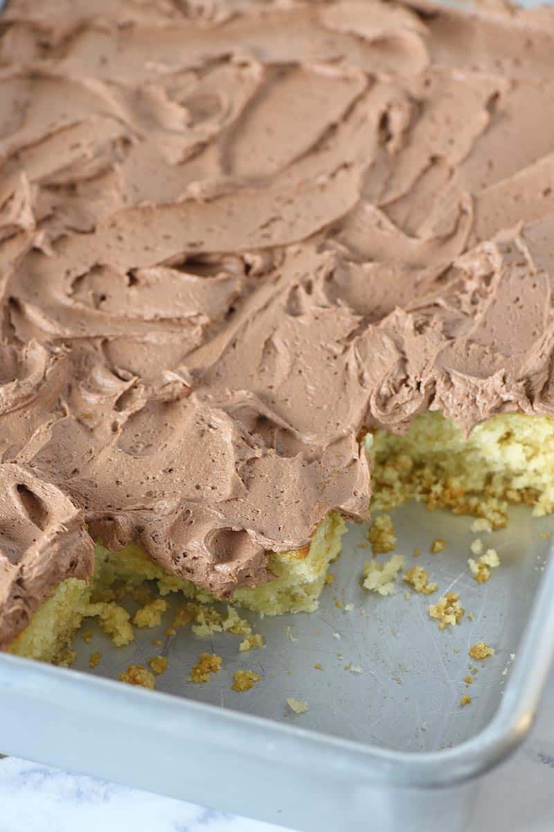 chocolate buttercream icing on sliced yellow cake in metal cake pan