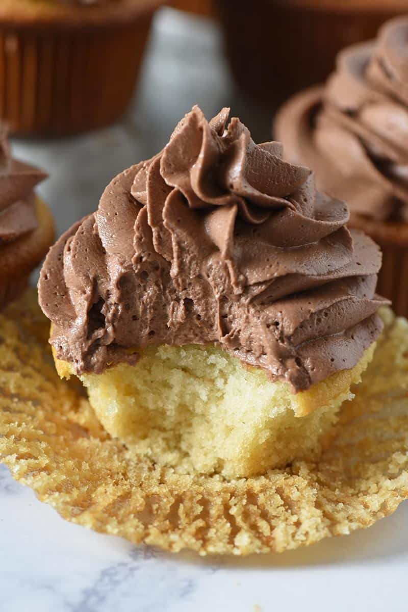 bite taken out of yellow cake cupcake frosted with homemade chocolate frosting