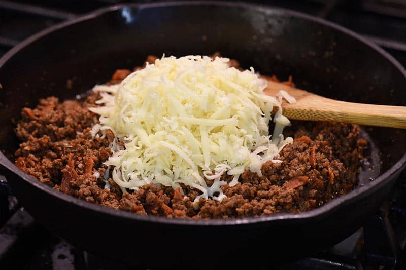 adding mozzarella cheese to pizza sloppy joes meat in iron skillet