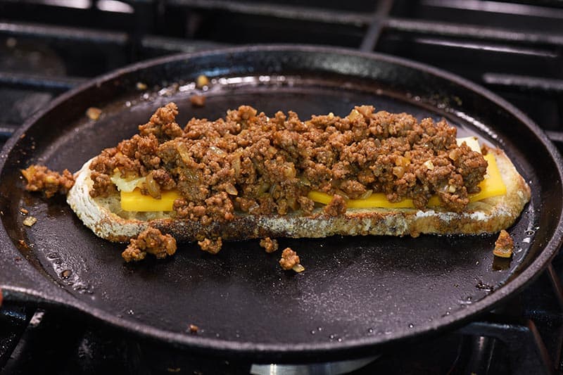 open grilled cheese with juicy burger meat on sourdough bread on cast iron griddle