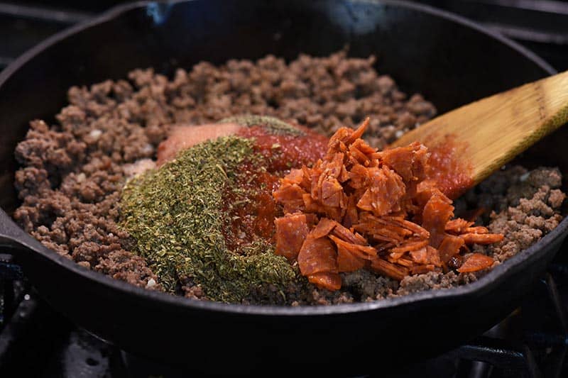 ingredients for pizza sloppy joe sauce in iron skillet with wooden spatula