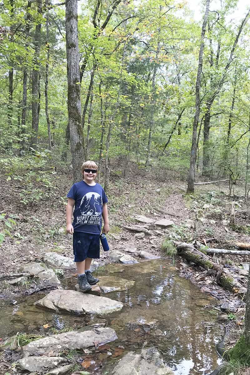 boy crossing over stream on Seven Hollows Trail in Petit Jean State Park
