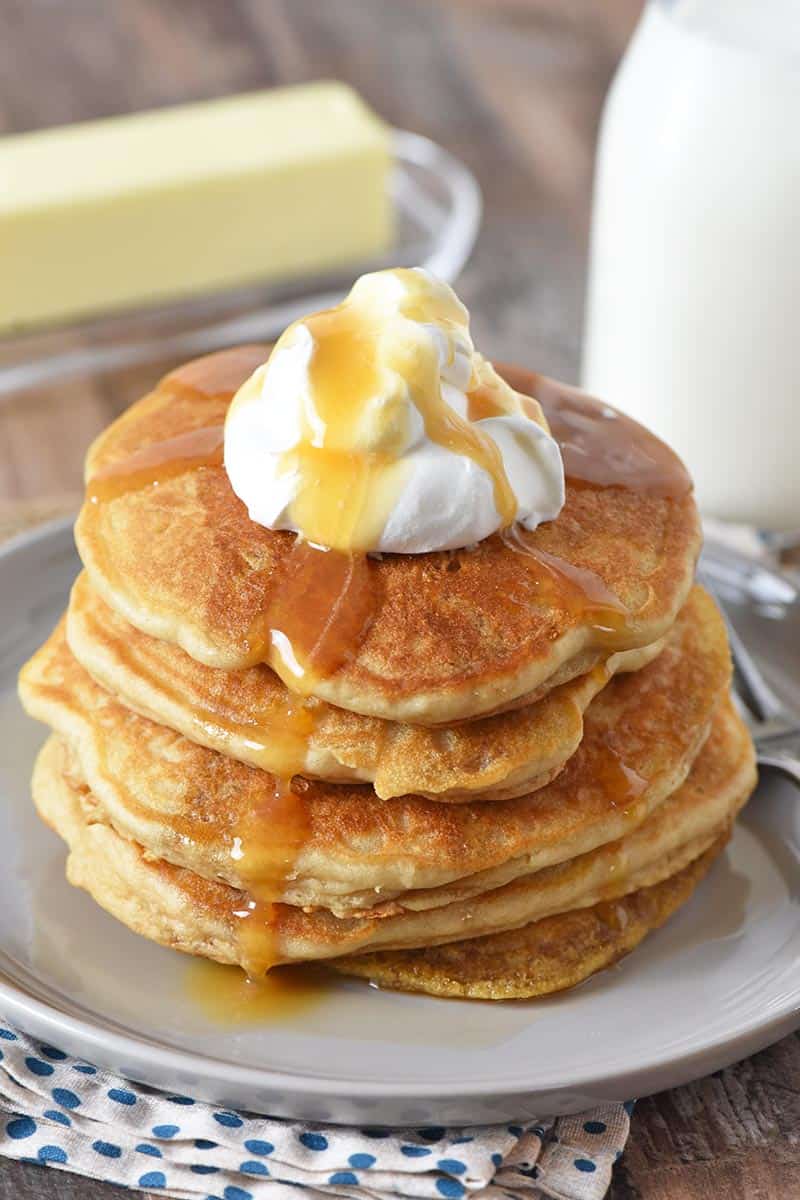 stack of homemade butterbeer pancakes from scratch on gray plate with whipped cream and butterscotch syrup and milk