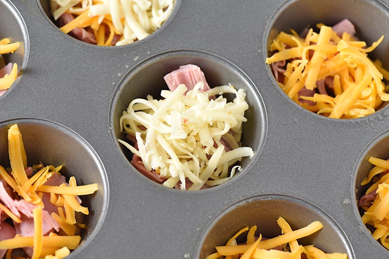 adding cheese with ham to muffin cups for breakfast egg muffins