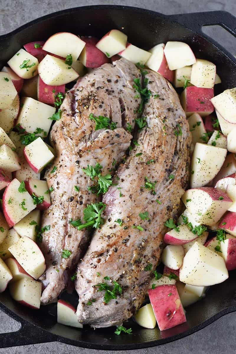 seared pork tenderloin with raw potatoes in cast iron skillet