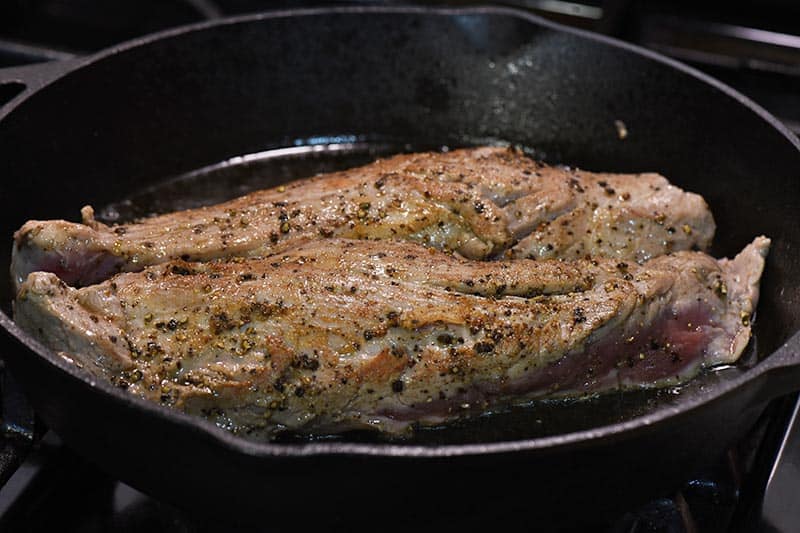 searing pork tenderloin in cast iron skillet on stovetop