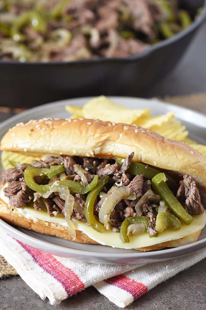 Cheesesteak sandwich on hoagie bun with provolone cheese, on gray plate with potato chips