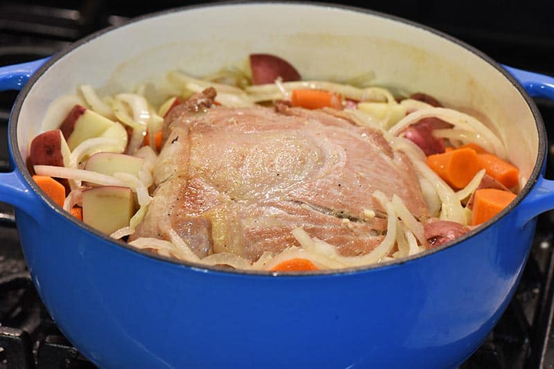 cooking pork roast with vegetables in blue Dutch oven