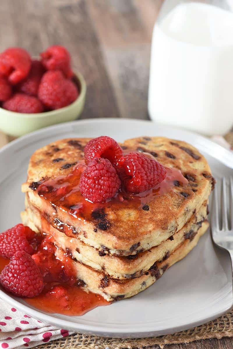 heart shaped pancakes with chocolate chips, raspberries, and sauce on gray plate