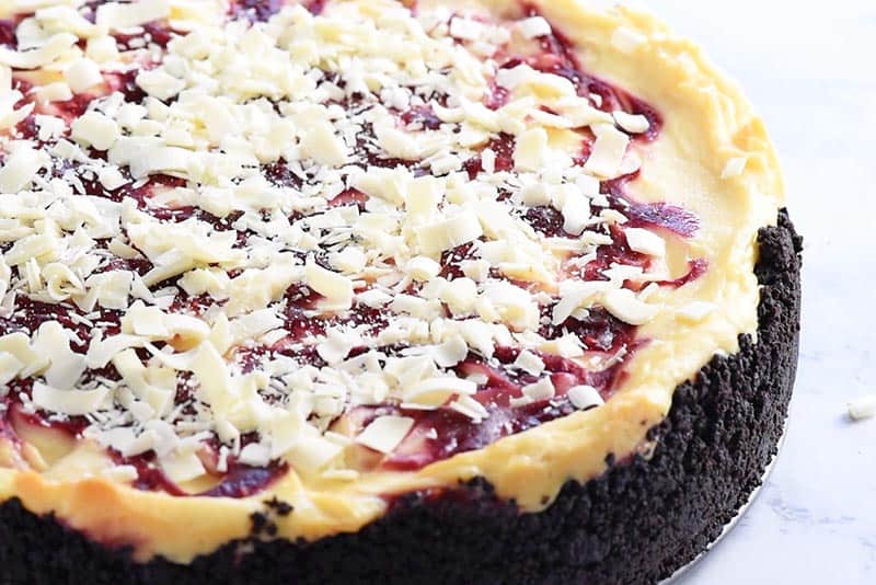 sprinkling shredded white chocolate onto top of white chocolate raspberry cheesecake