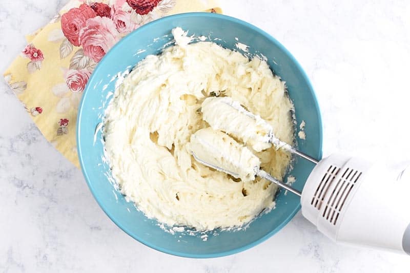 mixing cheesecake batter in blue bowl with white hand mixer