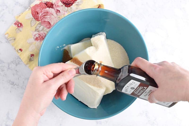 adding cheesecake ingredients, including Watkins Baking Vanilla, to blue mixing bowl