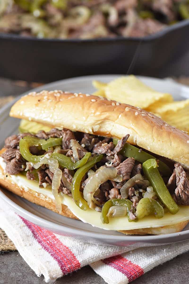traditional Philly cheesesteak sandwich with provolone cheese, served on gray plate with potato chips