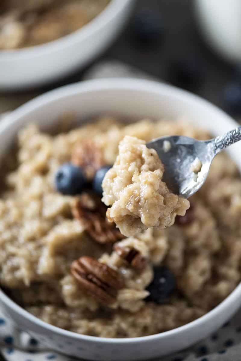 spoonful of maple and brown sugar oatmeal above white bowl of oatmeal with pecans and blueberries