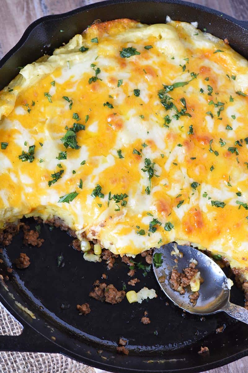 sloppy joe casserole with potatoes, covered with melted cheese and parsley in cast iron skillet with serving spoon