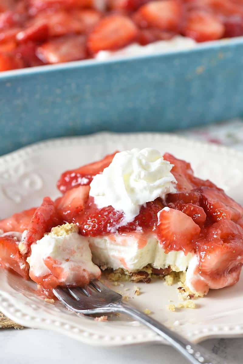 slice of strawberry yum yum on white plate with bite of no bake Dream Whip cream cheese filling, berries, and pie crust on fork