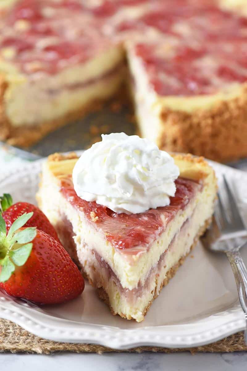 slice of strawberry cheesecake with whipped cream and strawberries on a white plate with a fork