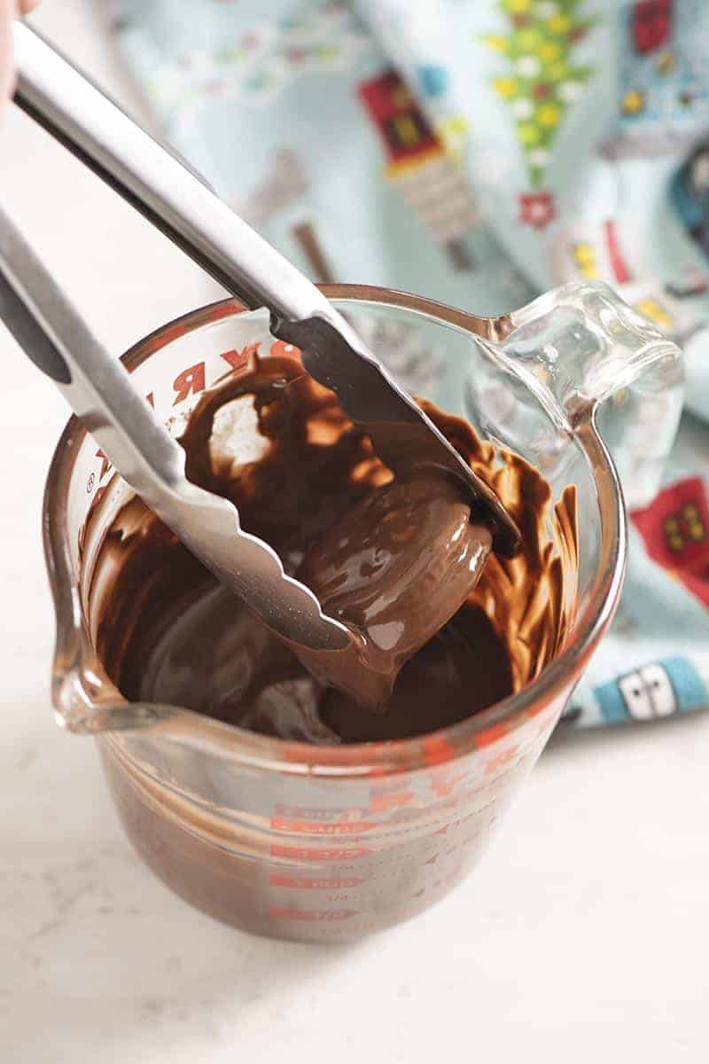 making Ritz crackers with peanut butter dipped in chocolate using Pyrex glass measuring cup and tongs