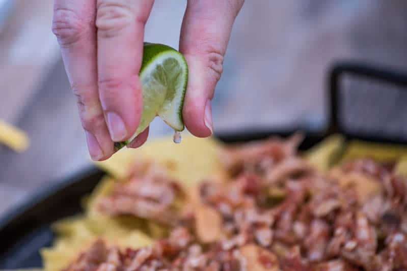 spritzing fresh lime juice on top of cheesy nachos