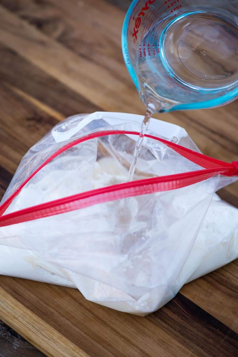 pouring lukewarm water into flour and yeast mixture for homemade pizza dough