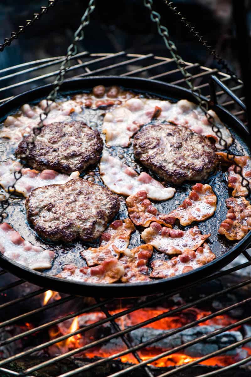 cooking burgers and bacon on griddle and tripod grill over campfire