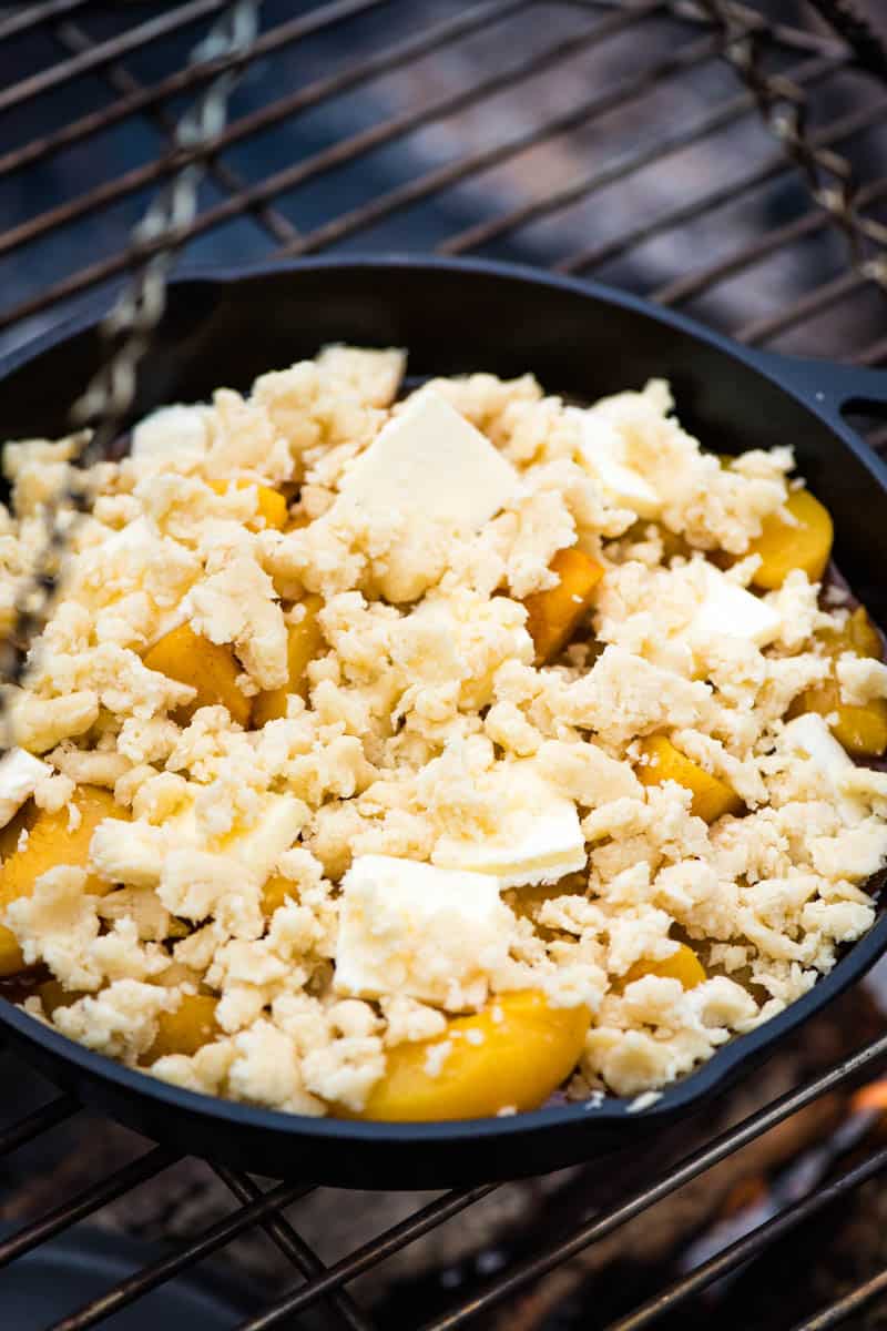 uncooked old fashioned peach cobbler in cast iron skillet on tripod grill over campfire