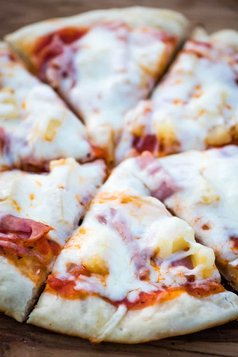 sliced ham and pineapple pizza on a wooden cutting board