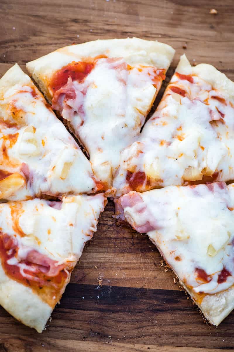 sliced campfire pizza with pineapple and ham on a wooden cutting board