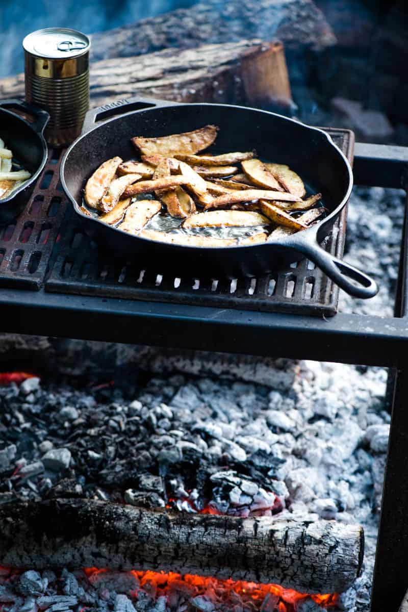 cooking steak cut fries in a cast iron skillet over the campfire on a campfire grill