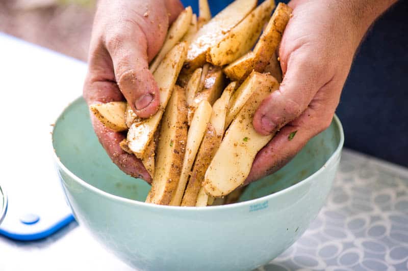 making seasoned steak fries by coating potatoes with olive oil and seasonings in large bowl