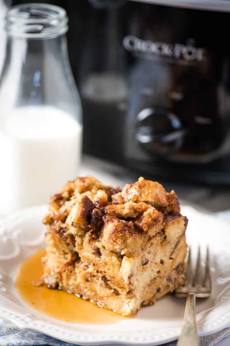 slice of slow cooker French toast breakfast casserole on white plate with fork, with black Crock Pot slow cooker in background