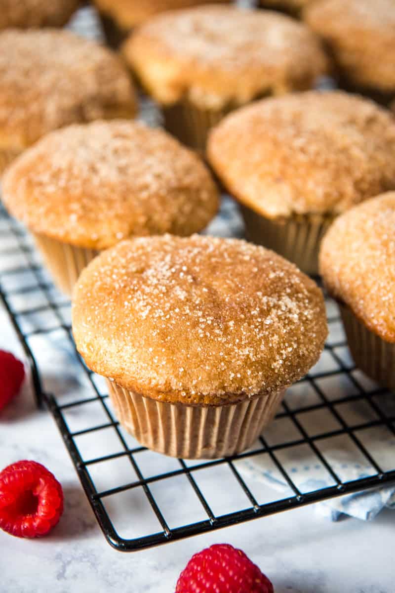 Bisquick sweet muffins sitting on wire rack, with fresh red raspberries on white marble countertop