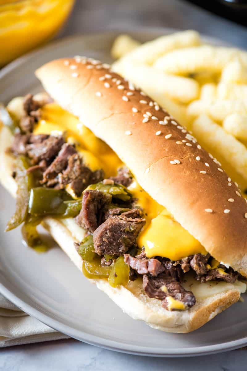 Crock Pot Philly cheesesteak sandwich filled with cheesesteak, provolone cheese, green bell peppers, and Cheez Whiz on gray plate with white Cheetohs