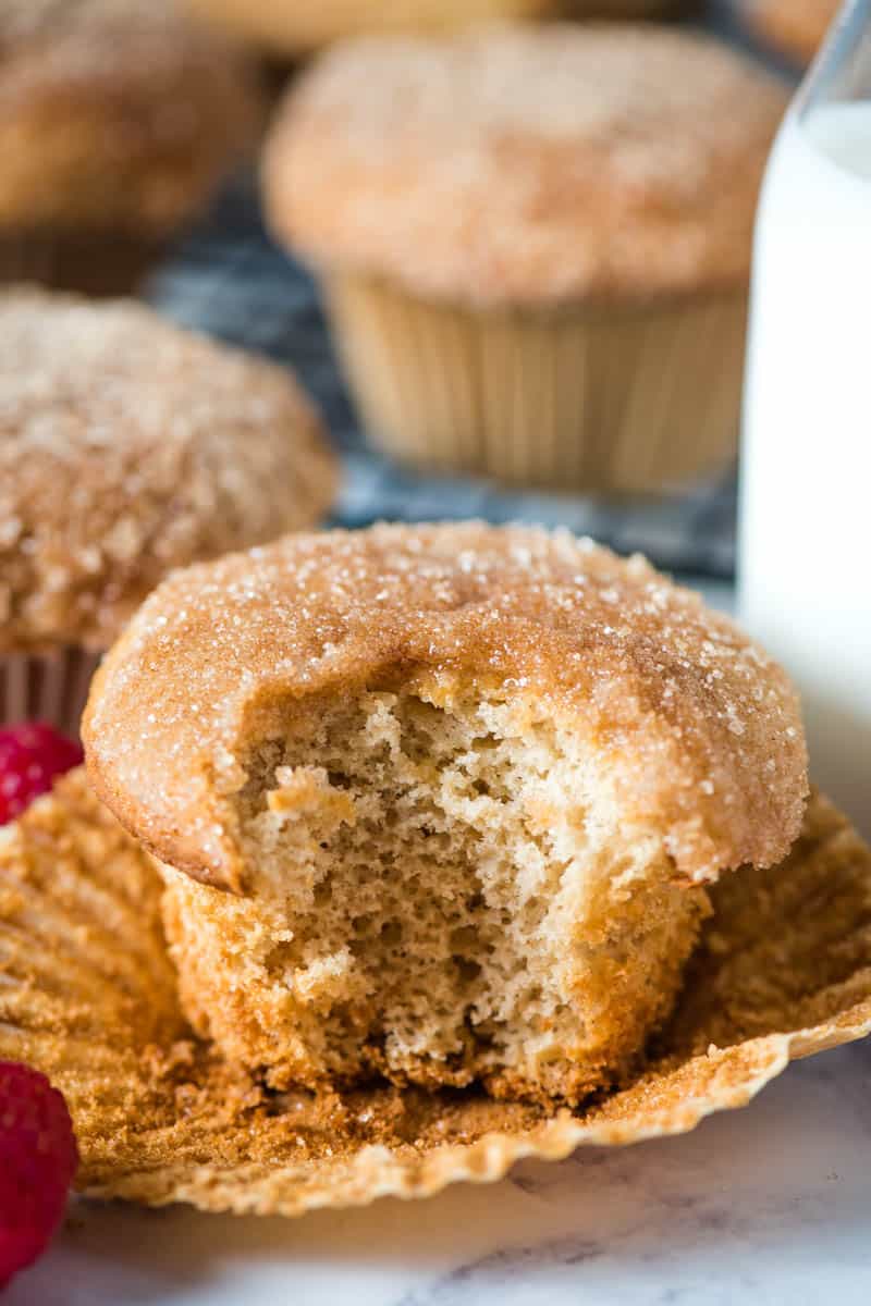bite out of sweet biscuit mix cinnamon muffin sitting on cupcake liner with fresh red raspberries and glass of milk
