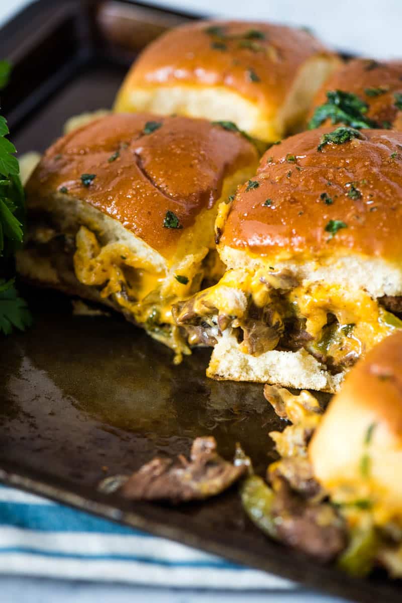 Philly steak sliders, sprinkled with Italian parsley and brushed with garlic butter, on metal baking sheet