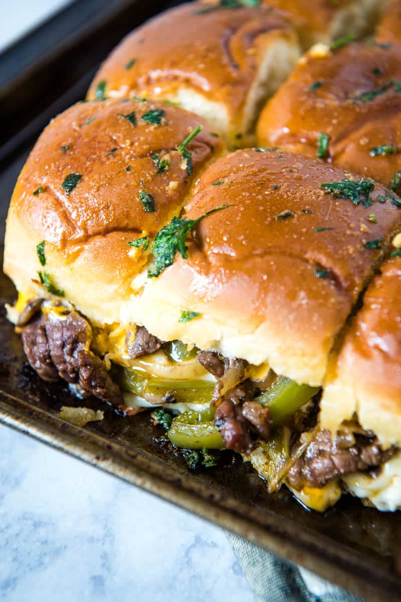 baked Philly steak and cheese sliders on Hawaiian rolls with green bell peppers and onions on metal baking sheet