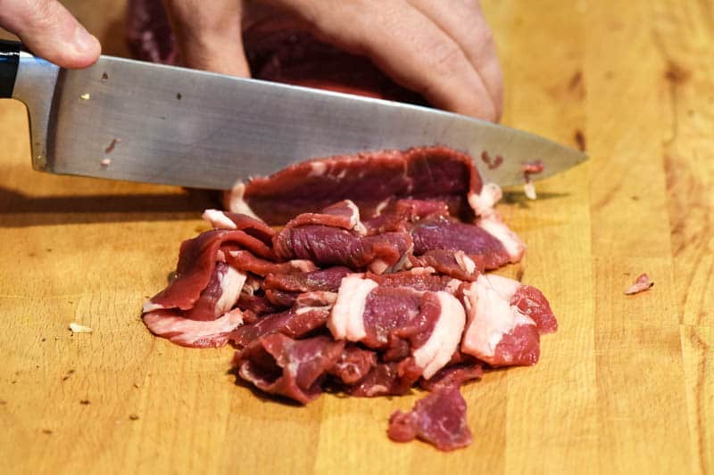 how to slice Philly cheese steak meat on wooden cutting board with chef's knife