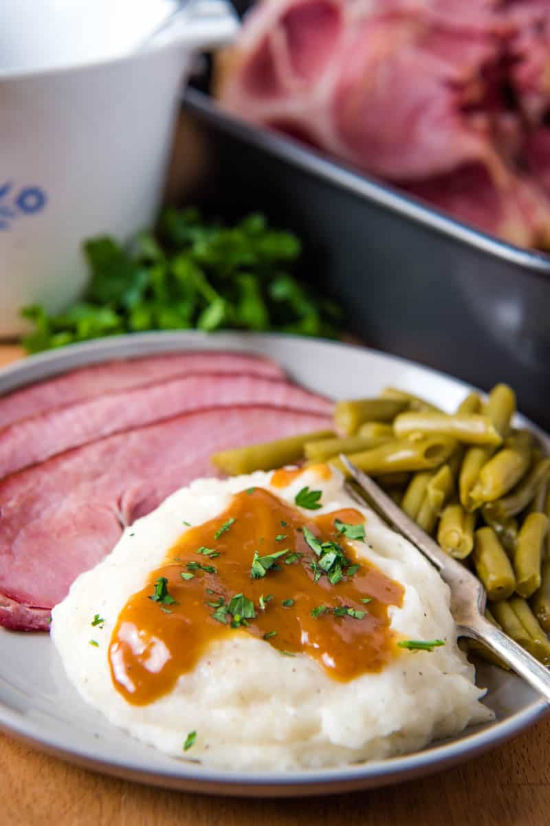 ham drippings gravy on mashed potatoes, served with sliced ham and green beans on gray plate with fork
