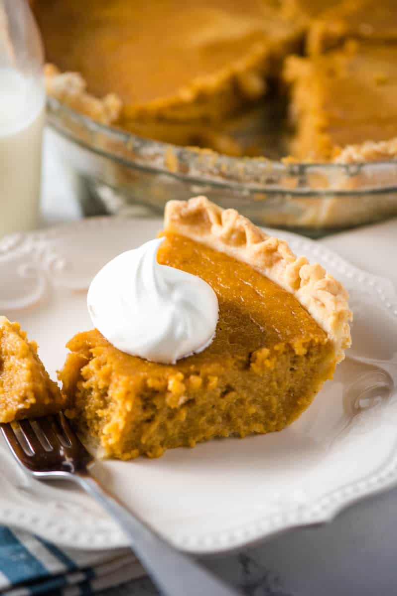 perfect pie crust with sweet potato pie filling and whipped cream on white plate with fork