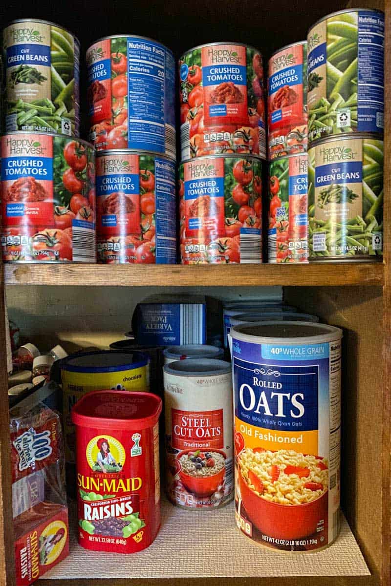 shelf-stable canned foods and survival foods in cabinet, including crushed tomatoes, green beans, oats, and dried fruit