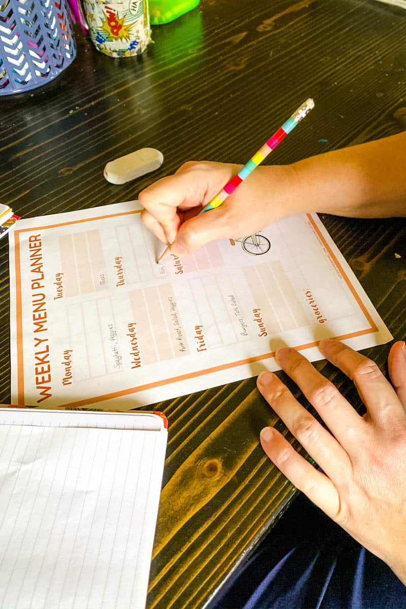 writing dinner ideas on a weekly meal plan with rainbow colored pencil