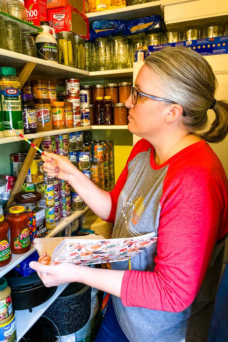 woman taking inventory of pantry staples with pencil and notebook in home working pantry