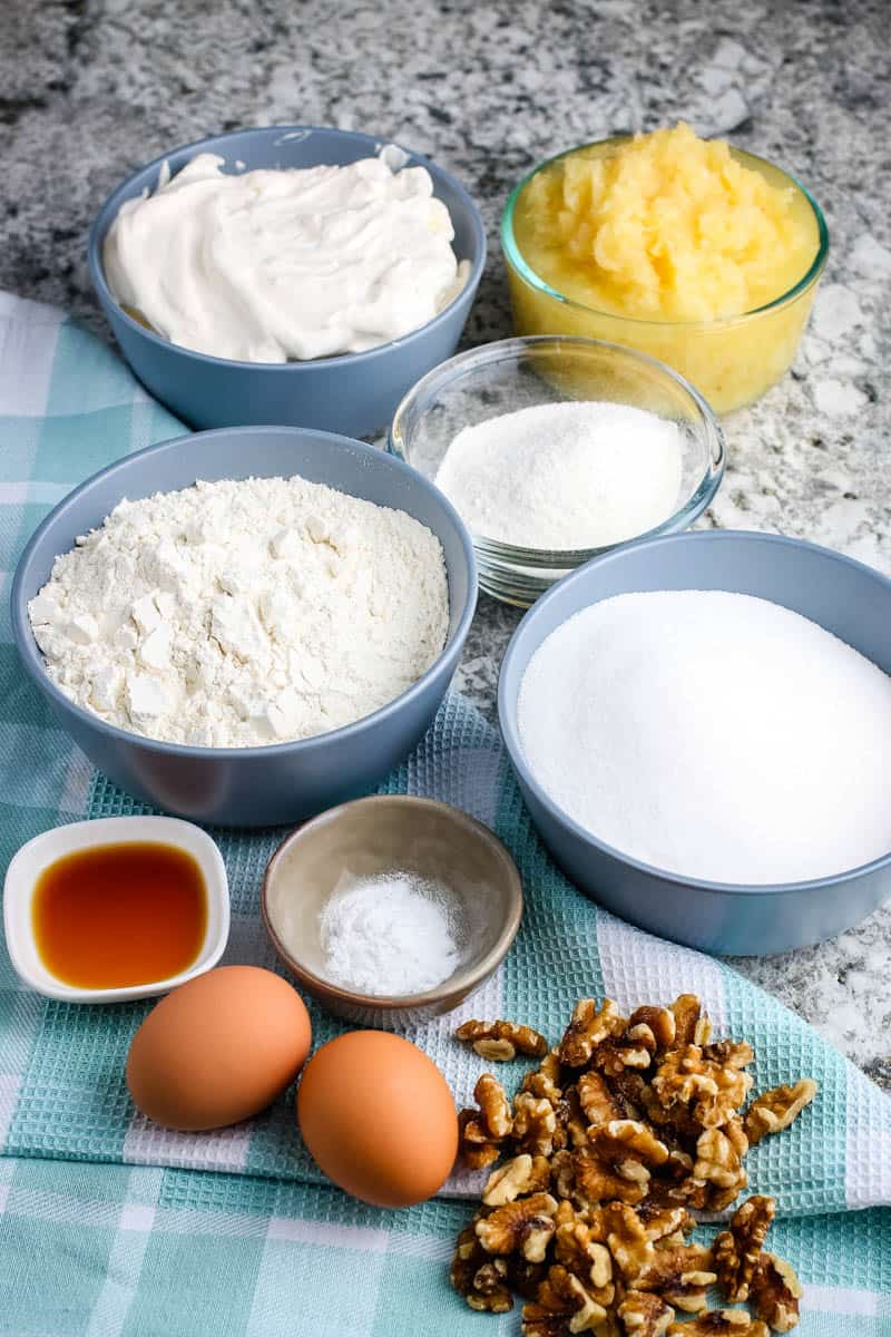 pineapple cake ingredients, including flour, sugar, baking soda, eggs, vanilla extract, crushed pineapple, walnuts, whipped cream, and vanilla pudding mix